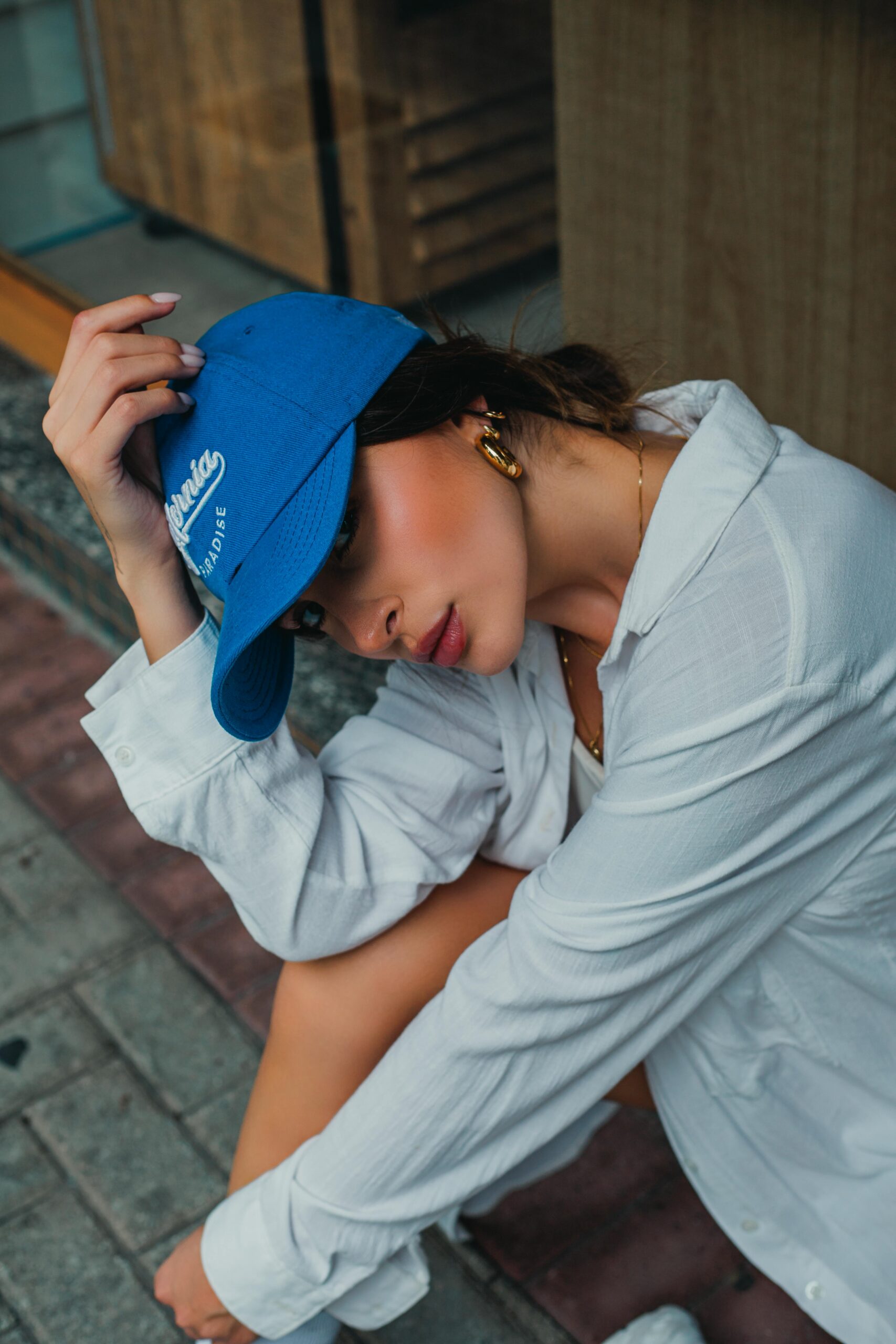 Stylish woman in blue cap and white shirt posing in an urban setting.